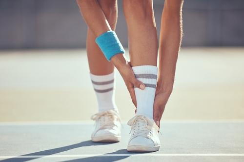 A tennis player holding her foot in pain due to repetitive stress injury.