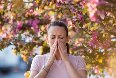 Sneezing young woman with her hands outdoor.