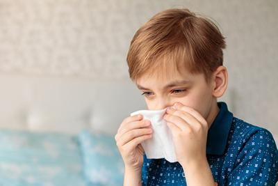 Young boy suffering from flu wiping his nose