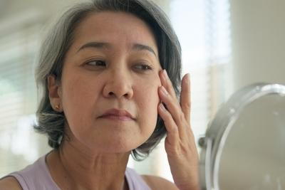 Older woman touching face while examining skin aging in mirror