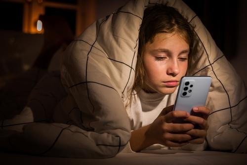 Child lying awake at night using a smartphone, unable to sleep