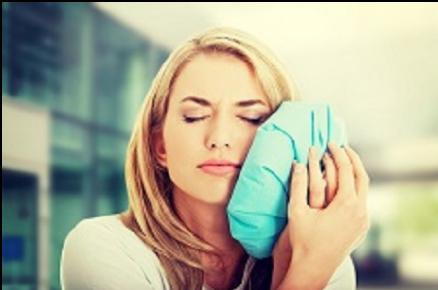 Woman in pain holding ice pack on left cheek needs root canal treatment