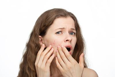 Woman noticing facial acne with shocked expression while examining her skin