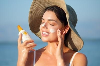 Smiling woman in hat applying sunscreen outdoors