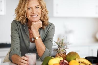Smiling woman with smoothie and fruits promoting good gut health