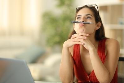 Young woman playing her ballpen in mouth.