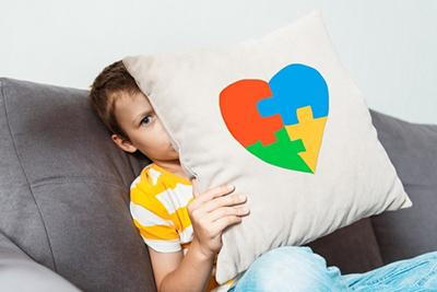 Young child holding a heart puzzle pillow with vibrant colors representing Autism Spectrum Disorder awareness.