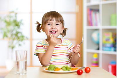 Young girl smiling on table while eating salad
