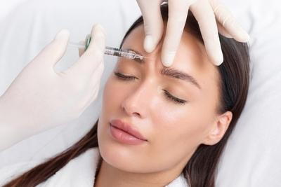 Injecting Botox in face of the woman with doctors hand in gloves.