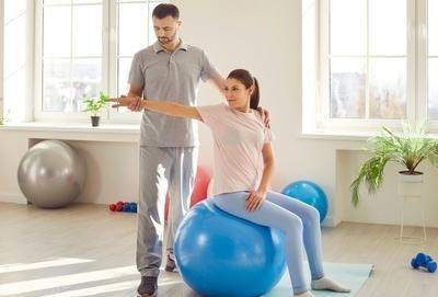 Therapist-massage-the-woman-hand-in-clinic-sitting-on-exercise-ball.