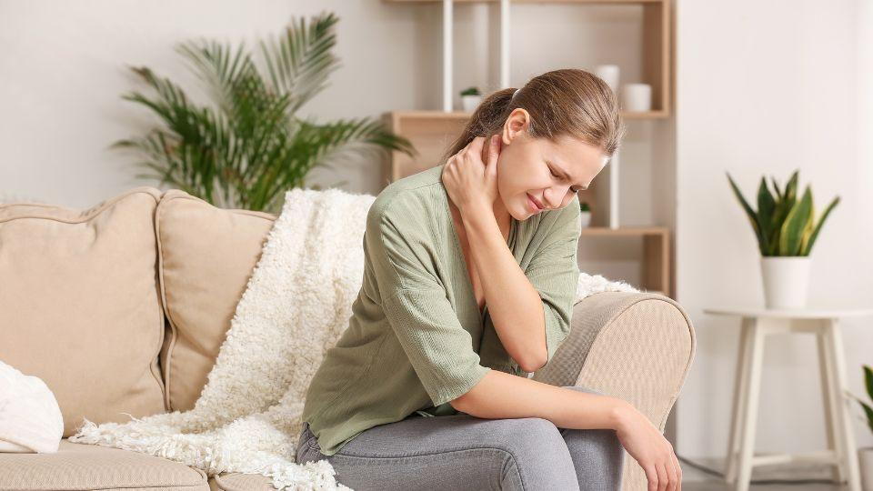 Woman Sitting On A Couch Holding Her Neck