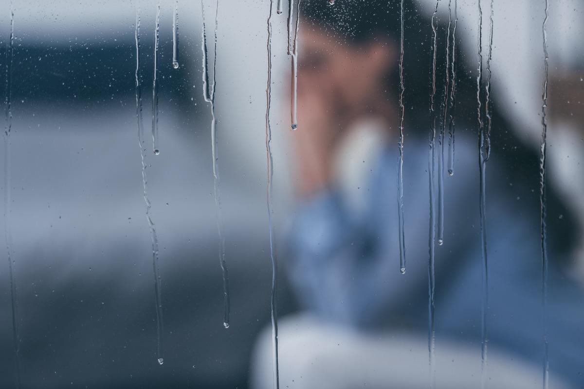 Behind a window covered in rain droplets sits a grieving woman.
