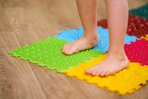 A child with flat feet walking on an orthopedic massage mat to support foot development.