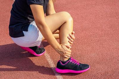 Woman outside holding her ankle in pain with black sneakers.