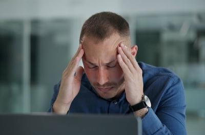 Man suffers migraine infont of the computer holding his head.