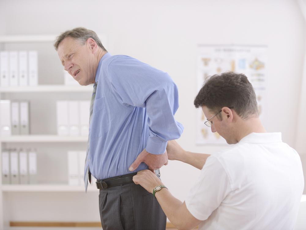 man with back pain is in a chiropractors office in Exeter