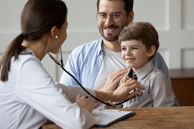 Pediatrician-using-stethoscope-on-happy-boy-with-dad.