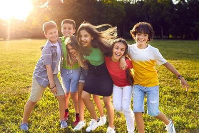 Smiling-Kids-Hugging-Outdoors-In-a-Sunny-Green-Park