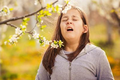 Young-girl-sneezing-outdoors-due to-pollen-allergies.