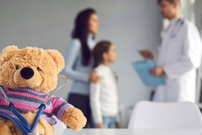 Mother with her daugther in the background with teddy bear infront.
