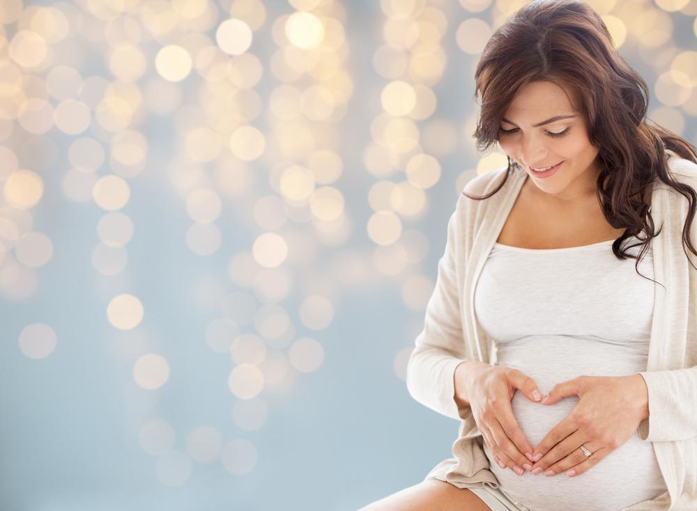 pregnant woman smiling, holding her hands on her belly after prenatal chiropractic care