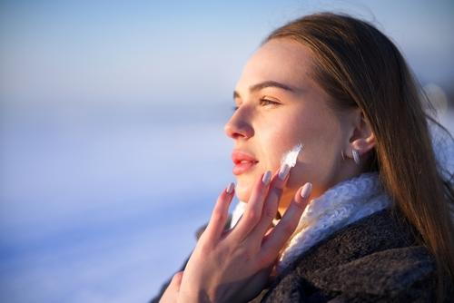 Woman applying moisturizer to her face for winter skin care.