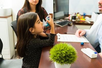 Young girl holding an inhaler and talking by the doctor with her mother on clinic.