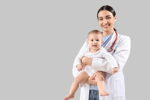 A pediatrician holding a baby against a neutral gray background.