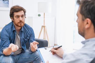 Young man talking to a therapist with notes sitting on sofa