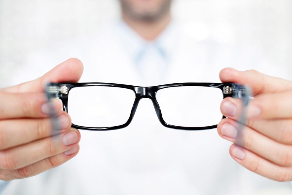 a person's hand holding a pair of eyeglasses. The person's fingers gently rest on the smooth surface of the glasses
