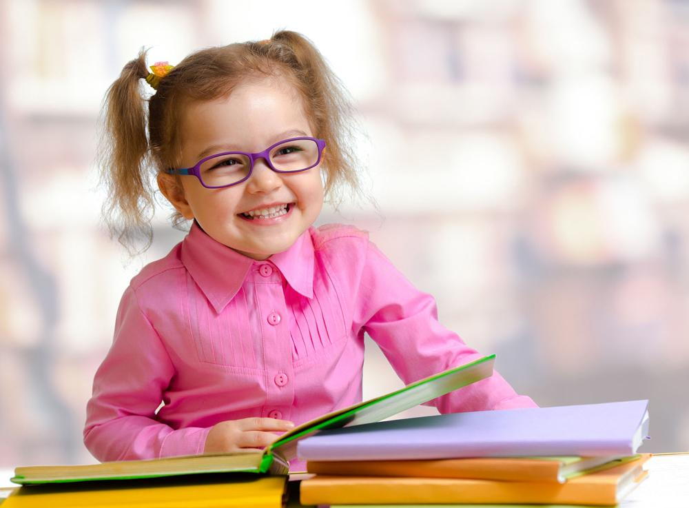a child with eyeglasses smiling at a book