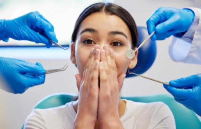 Four blue-gloved hands holding dental tools around a woman holding her mouth with her hands