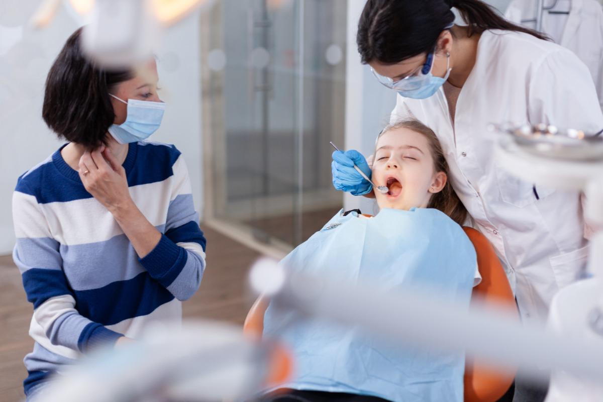 A child undergoes a dental exam by a dentist while her mother observes