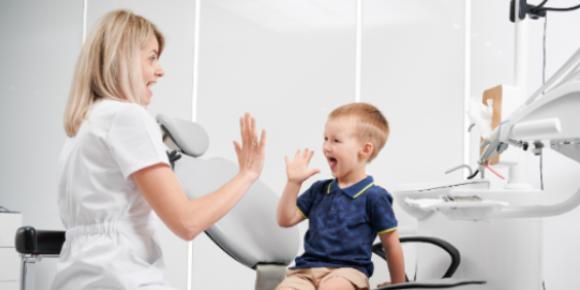 A young boy high-fives a female dentist in a dental exam room