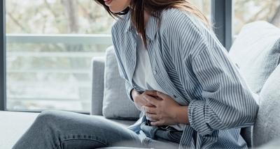 Woman holding her stomach in pain while sitting on sofa.