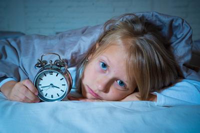 Little girl holding a clock, struggling to sleep at night