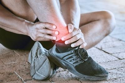 Runner-holding-his-ankle-in-pain-with-red-highlights-wearing-black-shoes.