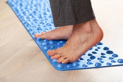 Man performing foot therapy exercises on an orthopedic massage mat