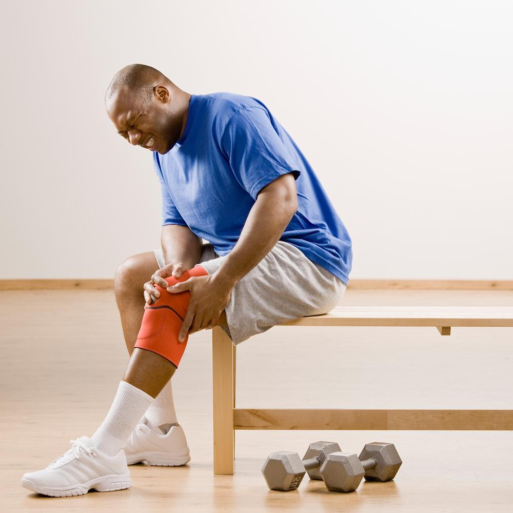 man sitting and holding his knee from pain form a sports injury, before seeking treatment from his Nanaimo chiropractor for injury prevention