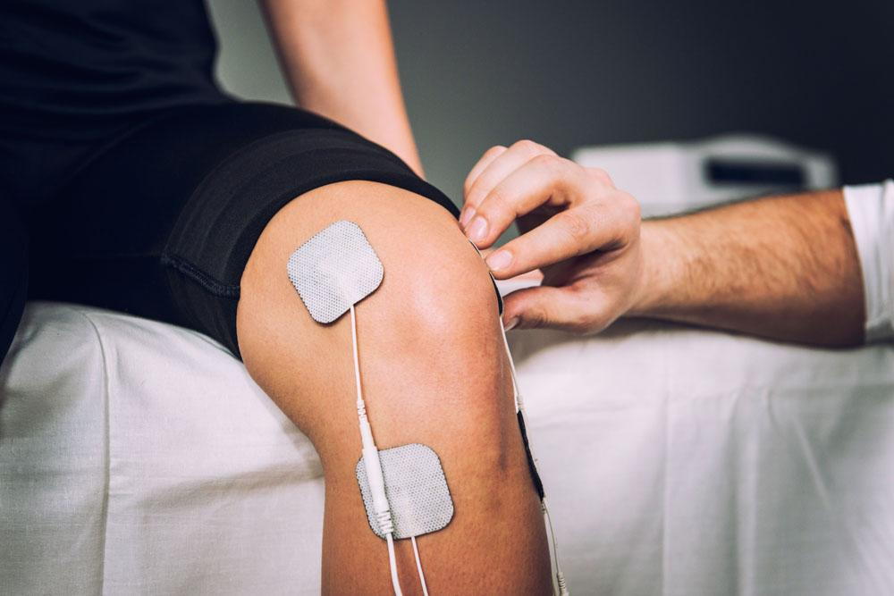 Physiotherapist in Nanaimo applying electrotherapy pads to a patient's knee during a physiotherapy appointment