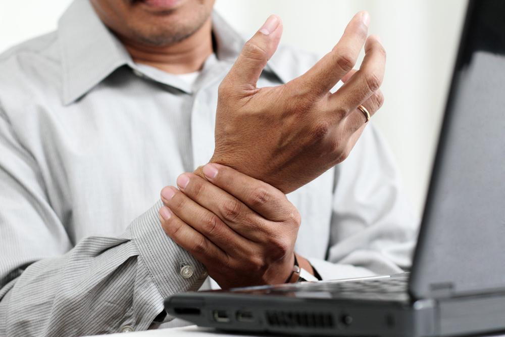 man at computer holding his wrist from carpal tunnel pain