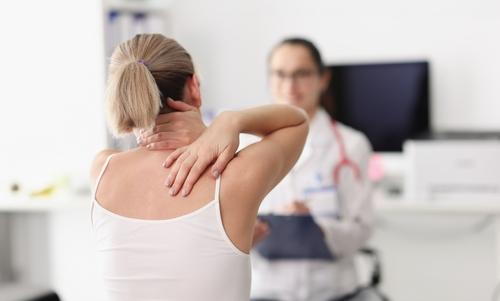 A woman holding her neck and back due to pain during a medical consultation.