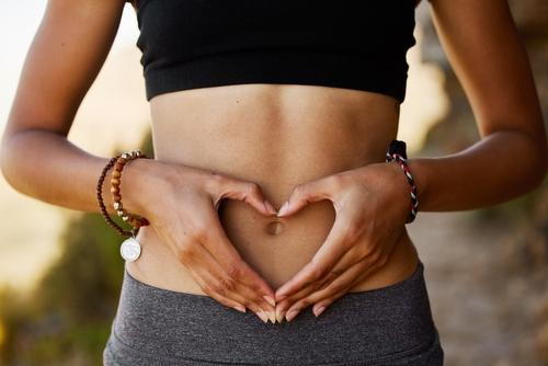 Female showing support for gut health with heart-shaped hands