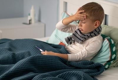 Young boy with fever holding his head and thermometer.