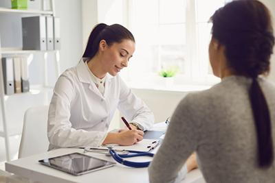 Woman doctor writing on notes with patient on clinic