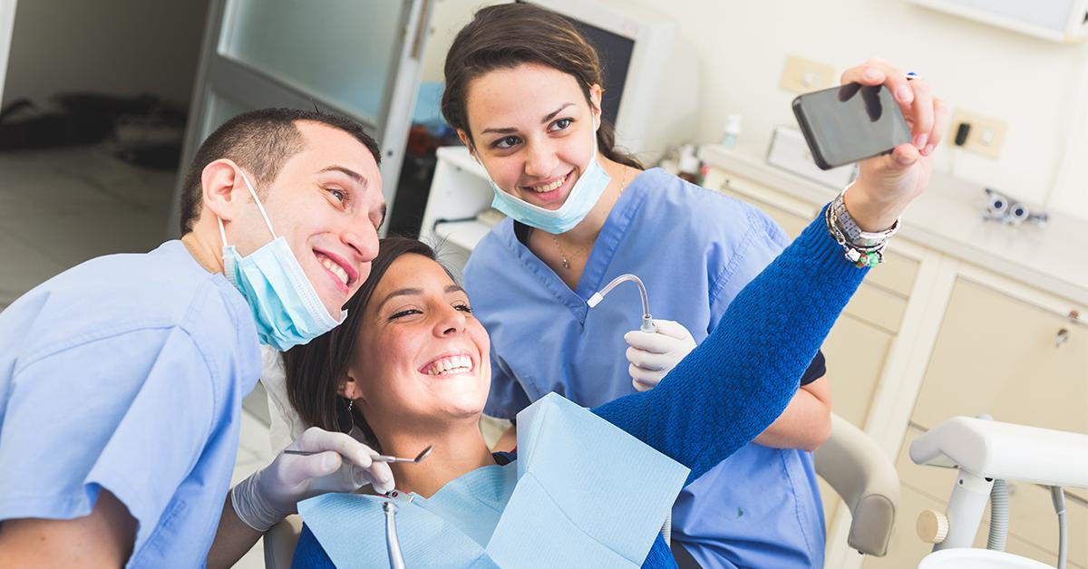 female dental patient taking a selfie with male and female dental professionals