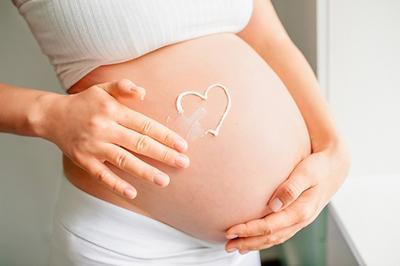 Pregnant woman draw a heart cream on her belly