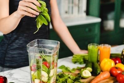 Person adding spinach to the blender with fresh veggies