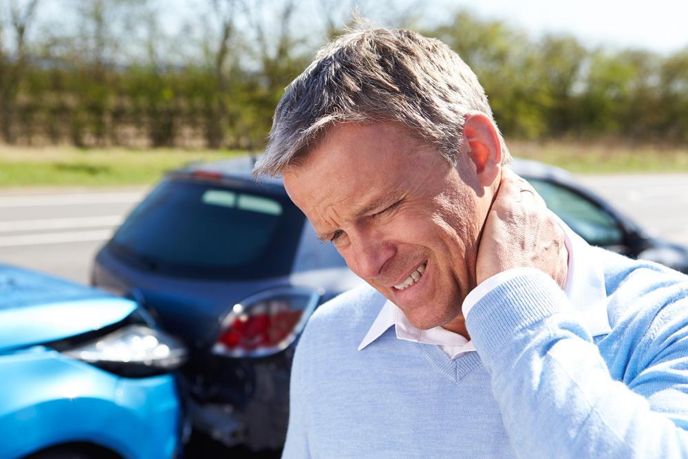 man holding his neck in pain with a car accident in the background