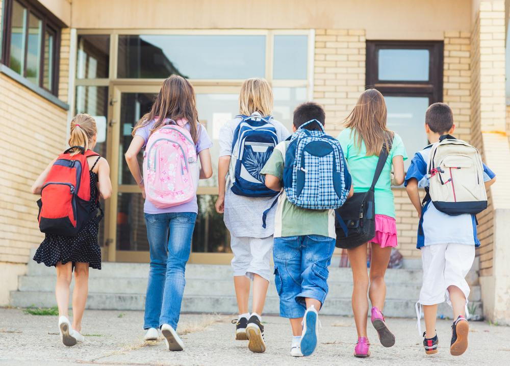 Kids wearing backpacks walking into school